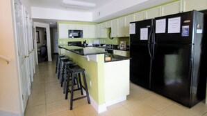 A kitchen with a central island, bar stools, a black refrigerator, and light green cabinets. - Coconut Grove - 403 (North Myrtle Beach)