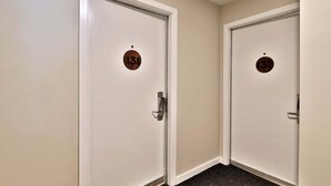 Deux portes blanches, portant les numéros 131 et 132, un sol recouvert de moquette et un mur sobre.