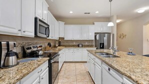 A modern kitchen with white cabinets, granite countertops, stainless steel appliances, and a tiled backsplash. - Cup8949 (Kissimmee)