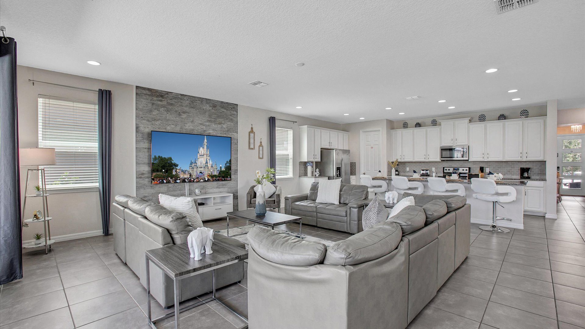 A modern living room with a sectional sofa, a coffee table, and a flat-screen TV mounted on the wall.