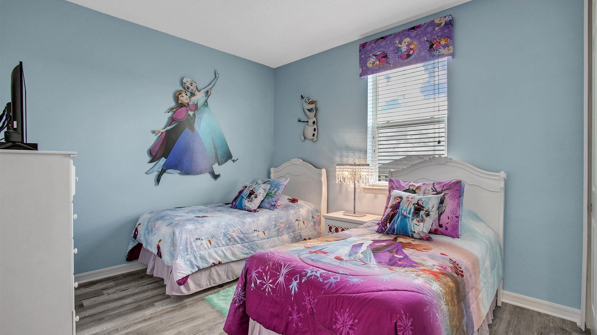 Une chambre avec deux lits, une commode, une table de chevet, une fenêtre avec des stores et une fresque murale.