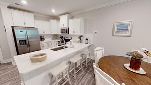 A modern kitchen with white cabinetry, stainless steel appliances, and a wooden dining table with a swan decoration. - Crow Creek 1706 (Calabash)