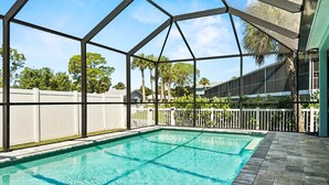 A covered swimming pool with clear water, surrounded by a white fence and trees. - Coastal Oasis 3 (Nokomis)