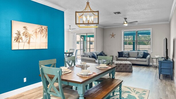 A dining area with a wooden table and chairs, a ceiling fan, and a starfish decoration on the wall. - Coastal Oasis 3 (Nokomis)