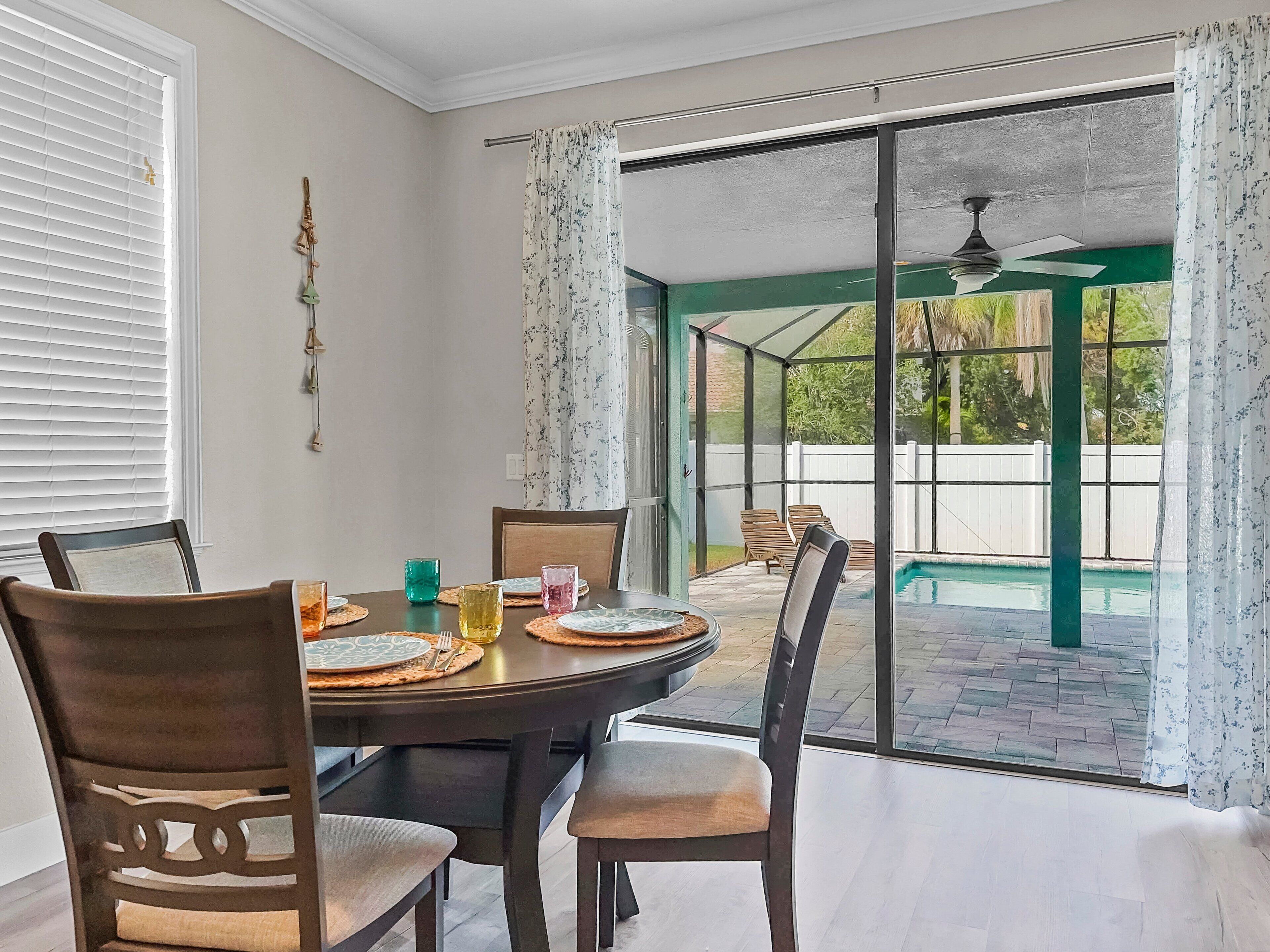 Un comedor con una mesa lista para cuatro personas, sillas y vista a un jardín con piscina.