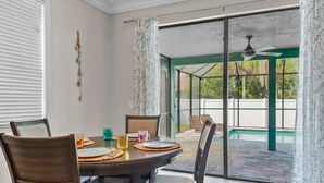 A dining area with a table set for four, chairs, and a view of a backyard with a pool. - Coastal Oasis 3 (Nokomis)