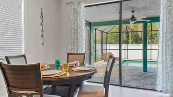 Un comedor con una mesa lista para cuatro personas, sillas y vista a un jardín con piscina.
