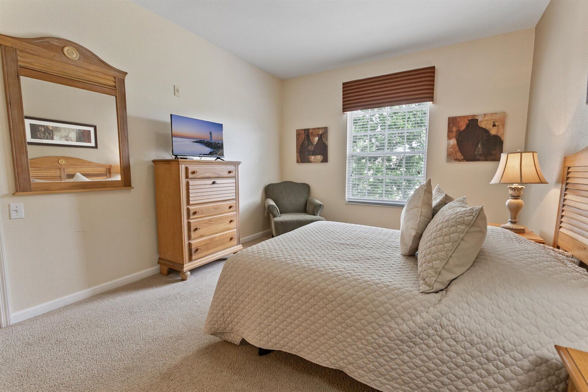 A bedroom with a bed, a dresser, a chair, a television, and artwork on the walls.
