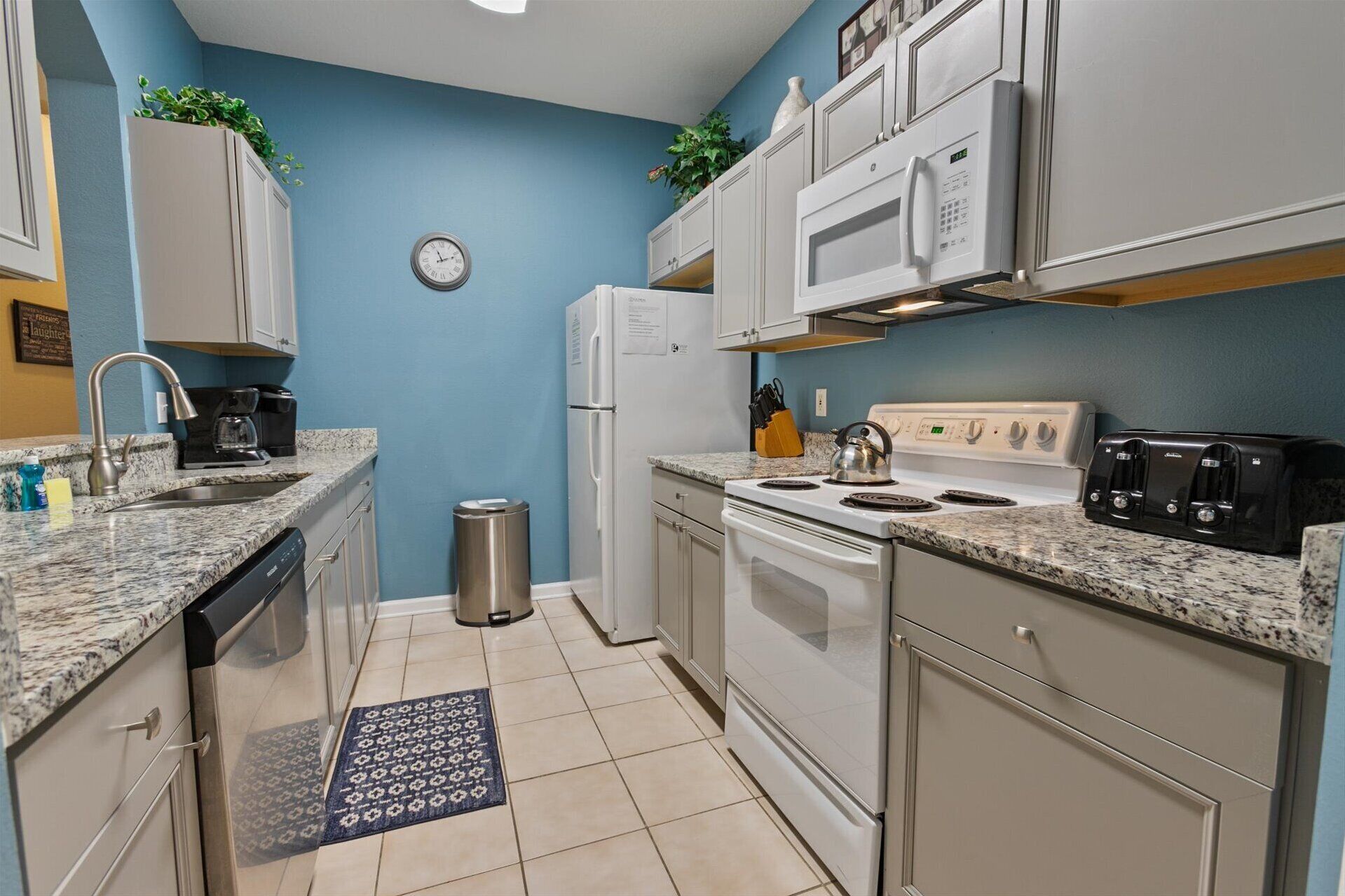 A compact kitchen with white cabinets, a stainless steel refrigerator, a microwave, a stove, and a sink.