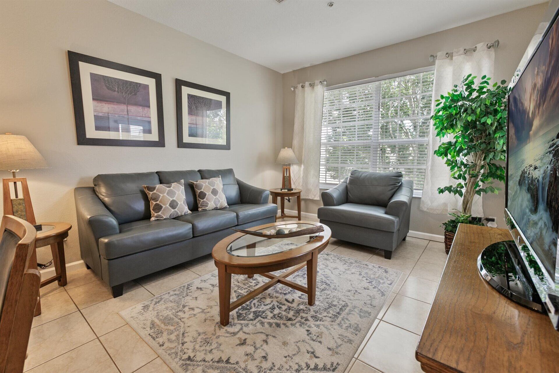 A living room with two sofas, a coffee table, a TV, and a large window with blinds.