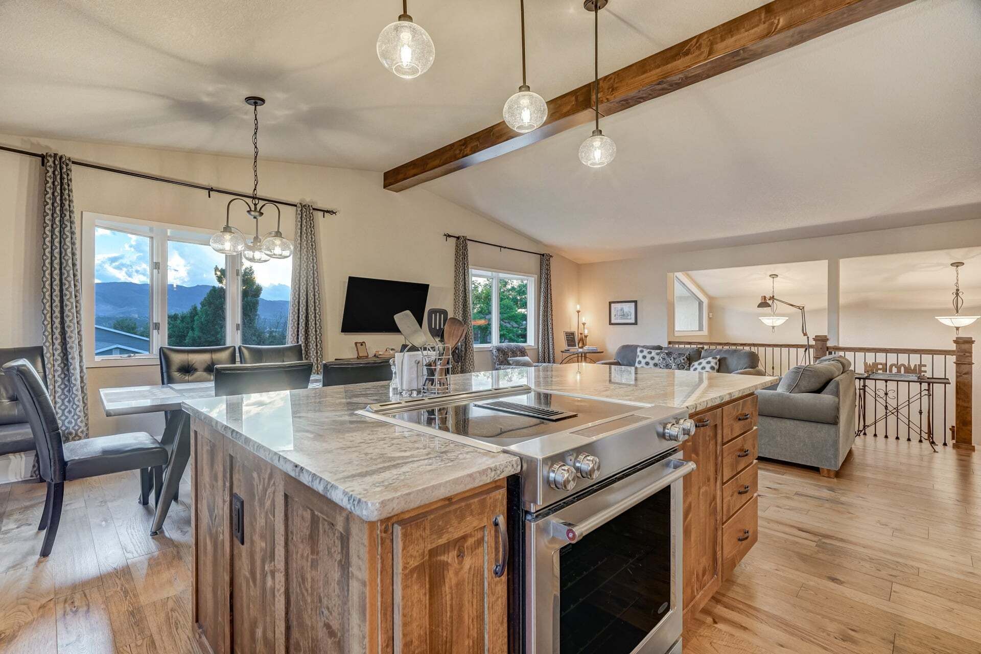 Una cocina amplia con una isla grande, armarios de madera y un horno empotrado. Hay un comedor con sillas y una mesa, y una sala de estar con sofá y televisor.