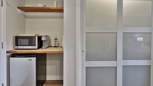 Una cucina compatta con forno a microonde, macchina da caffè e dispenser per l'acqua su un ripiano in legno.