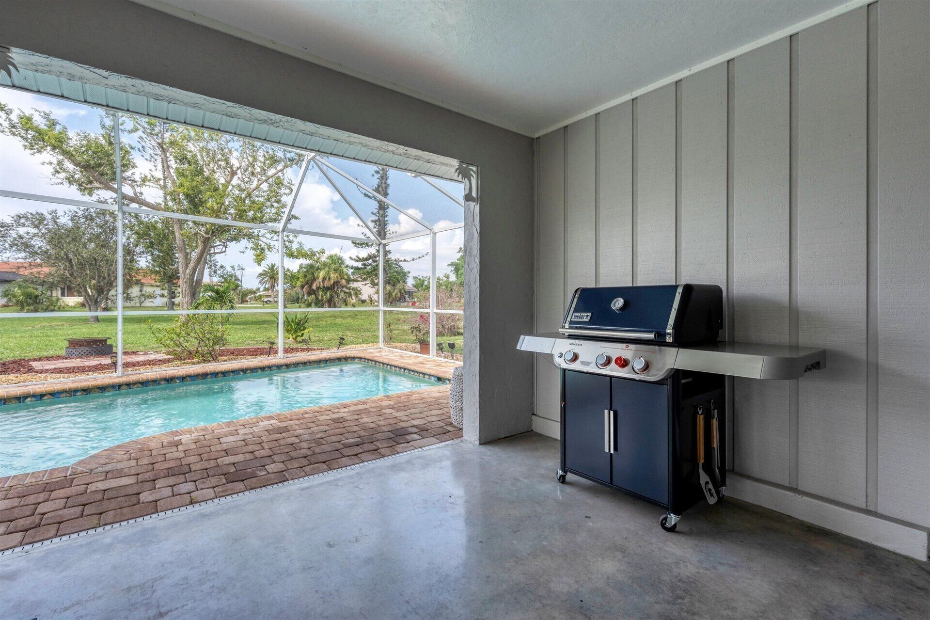 Un patio abrité avec une piscine, un barbecue et une vue sur un quartier résidentiel.