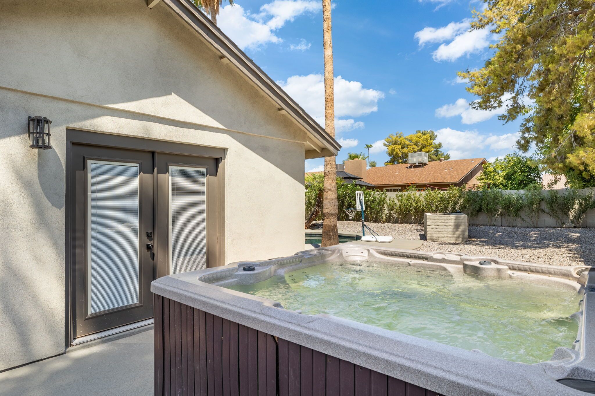 A spa area with a hot tub, a covered patio, and a building with a sliding glass door.