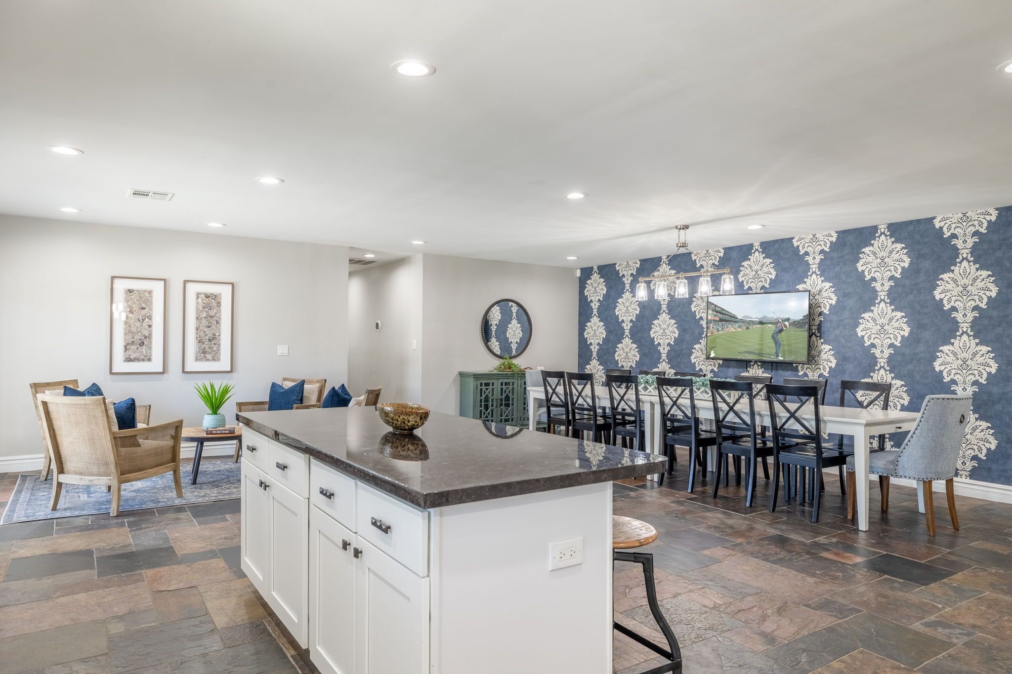 A modern kitchen with a central island, dining area with chairs and a table, and a patterned wall.