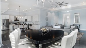 A modern kitchen with white cabinets, a dining area with a black table, and a living room with a grey sofa. - Ctd4751-401 (Kissimmee)