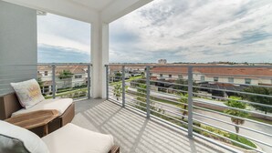 A balcony with a view of a residential area, featuring a wicker sofa, a small table, and a metal railing. - Ctd4751-401 (Kissimmee)