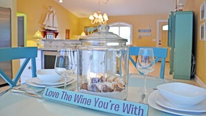 Ein Esstisch mit einem Glasbehälter voller Muscheln, einem Schild mit der Aufschrift 'Love The Wine You're With' und einem Schiffmodell an der Wand.