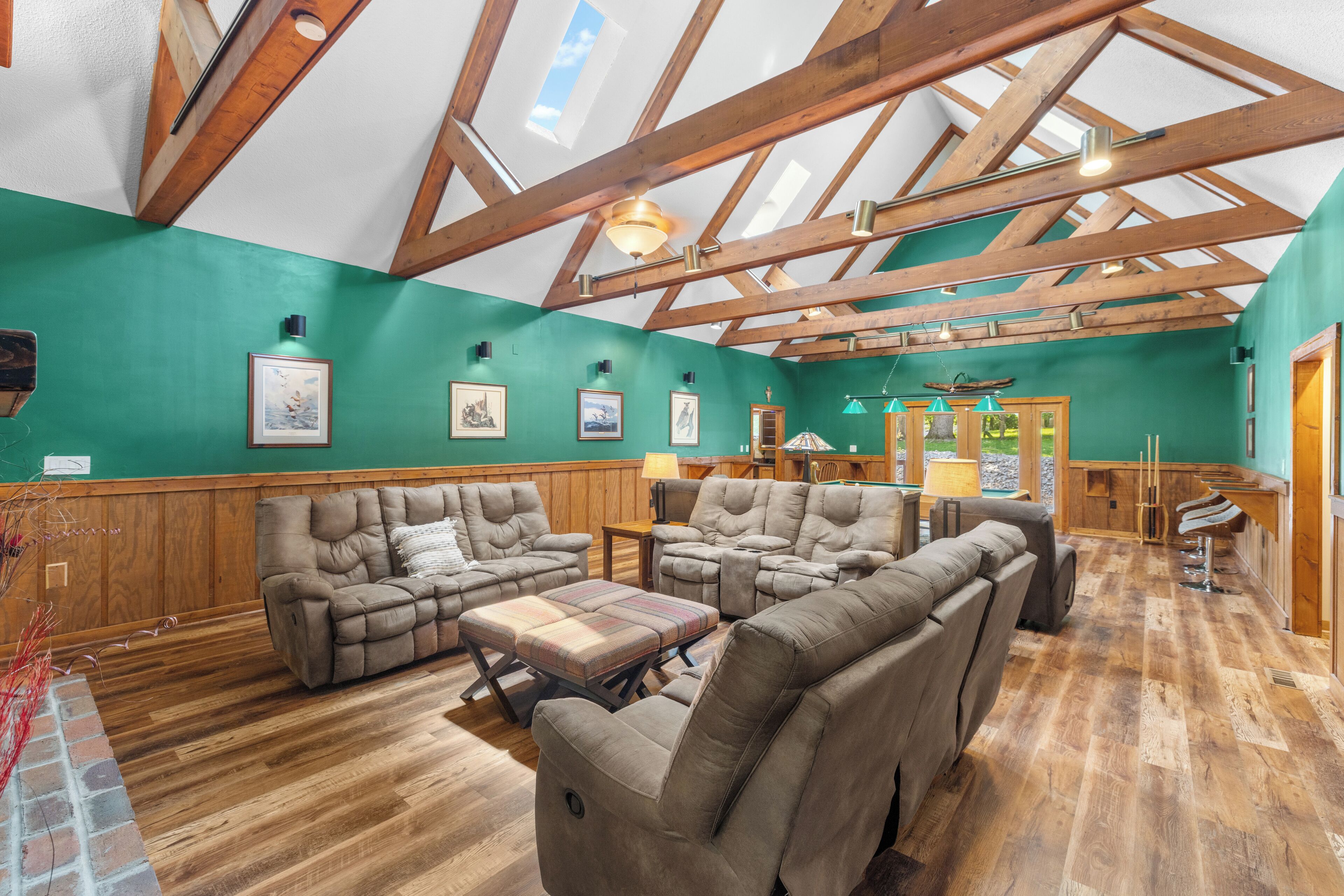 A spacious room with a high ceiling, wooden beams, and a green wall. There are multiple sofas and a dining table.