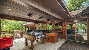 An outdoor patio with a barbecue grill, wooden deck, and glass doors leading to a covered area. - Cool Goose Landing Private Dock Large Deck Game Room 61 (Cadiz)