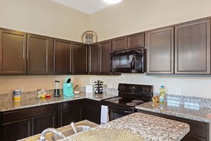 A kitchen with dark wooden cabinets, a black microwave, a stove, granite countertops, and a sink. - Cozy 3bd, 3BA Downtown Indy (Indianapolis)