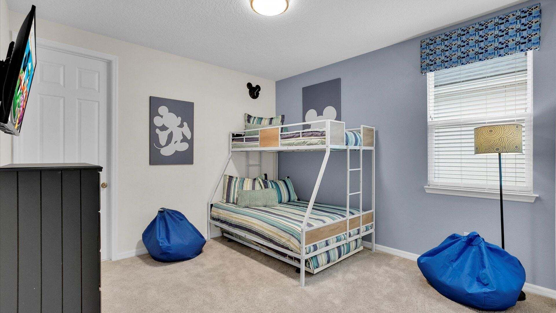 A bunk bed with a ladder, a desk, a chair, a bean bag, a wall clock, and a window with blinds.