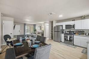 A modern kitchen with white cabinets, stainless steel appliances, and a dining area with a dark wooden table and blue plates. - Cozy 3BR Home Family-friendly Near Attractions (San Antonio)