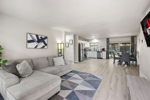 A modern living room with a grey sofa, a geometric rug, and a kitchen in the background. - Cozy 3BR Home Family-friendly Near Attractions (San Antonio)