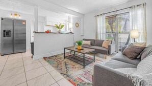 Un salon moderne avec un canapé gris, une table basse et un coin cuisine équipé d’un réfrigérateur et de placards.