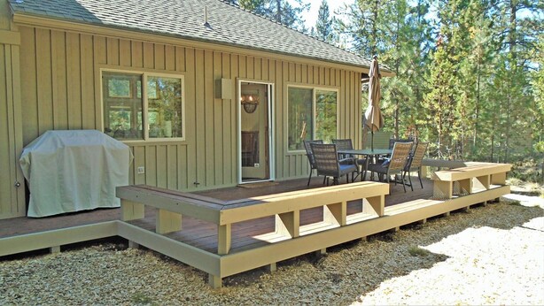 Une terrasse en bois avec une table et des chaises, un barbecue et un espace salon abrité.