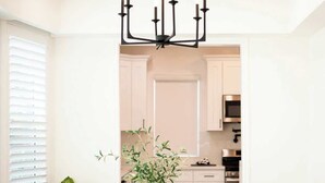 A dining area with a round table, four chairs, a chandelier, a potted plant, and a view into the kitchen. - Cozy Retreat Near Downtown Perfect for Families (Long Beach)