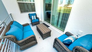 A sunlit patio with wicker furniture, a sliding glass door, and a white exterior wall. - Ctd4741-102 (Kissimmee)