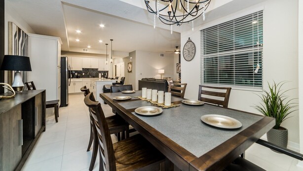 A modern kitchen with white cabinets, a dining area with a grey table set for four, and a large window with blinds. - Ctd4741-102 (Kissimmee)