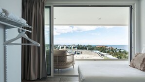 Een hotelkamer met een bed, een stoel en uitzicht op een strand en gebouwen.