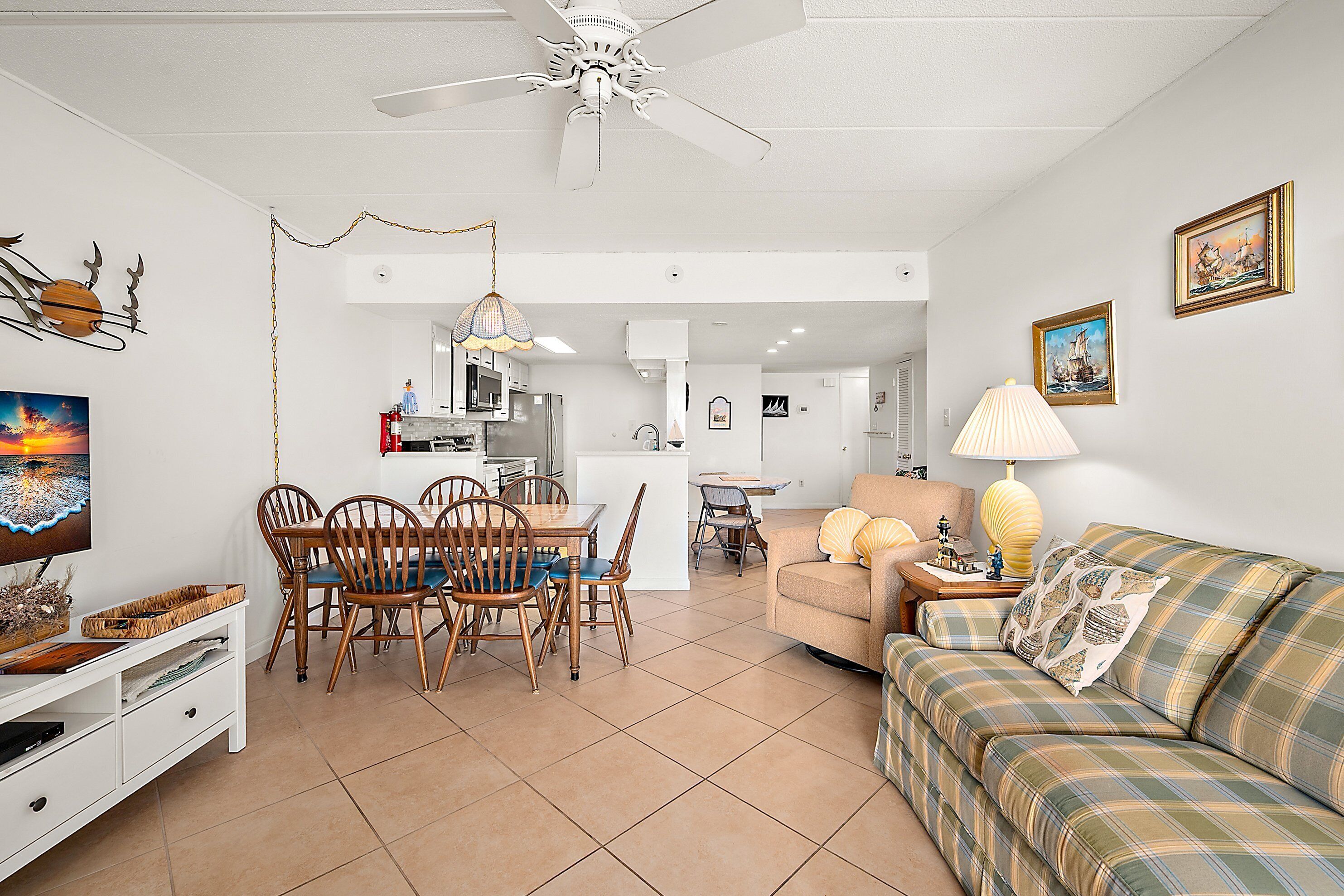 A spacious living room with a sofa, dining table, and chairs. There is a ceiling fan, a lamp, and artwork on the walls.