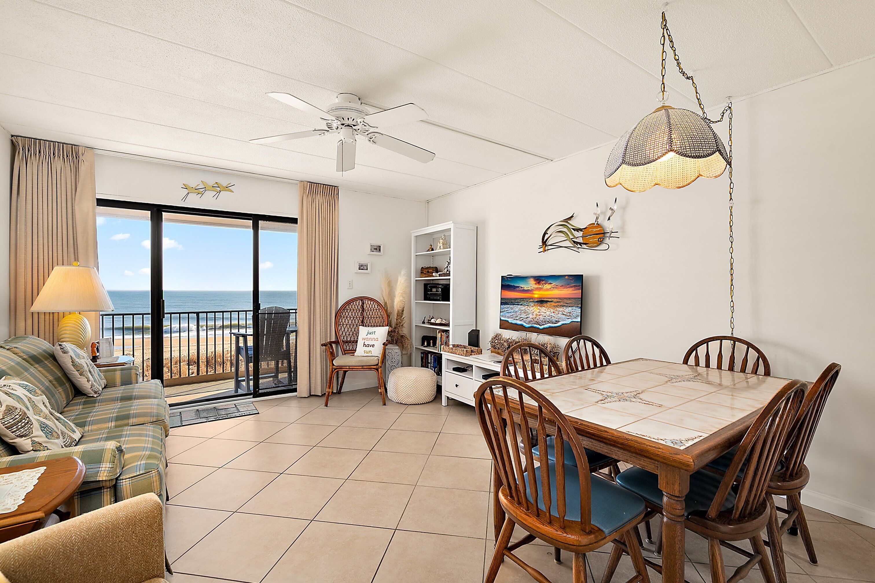 A spacious living area with a balcony, a dining table, and a ceiling fan.