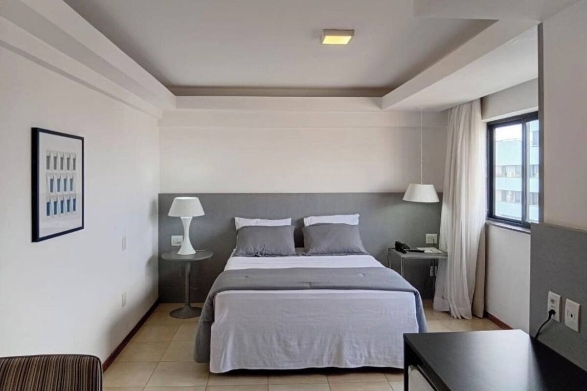 Ein modernes Hotelzimmer mit einem großen Bett, Nachttischen, einem Schreibtisch und einem Fenster mit Vorhängen.