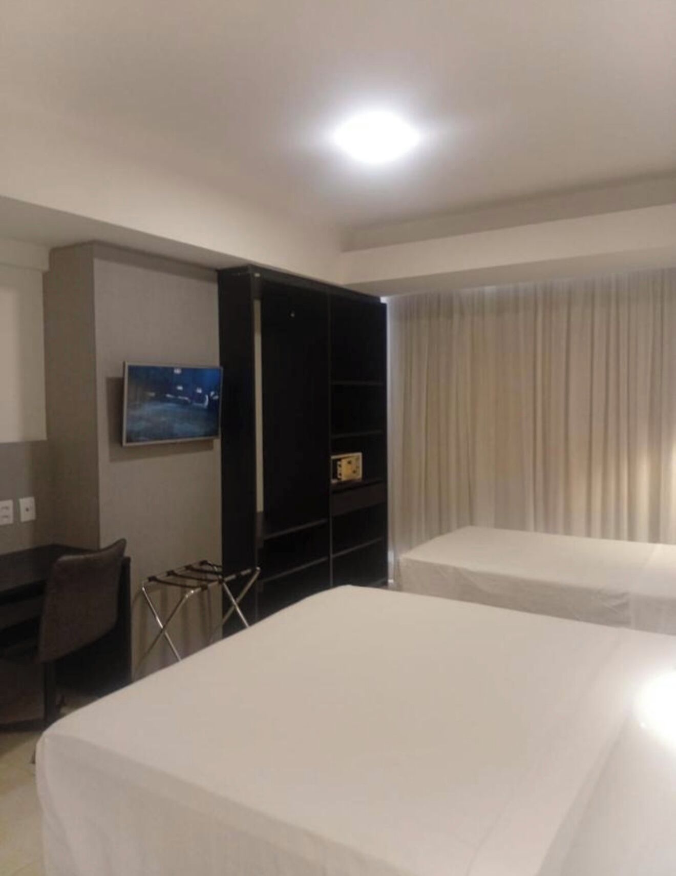 Quarto de hotel com duas camas, uma televisão na parede e um guarda-roupa.