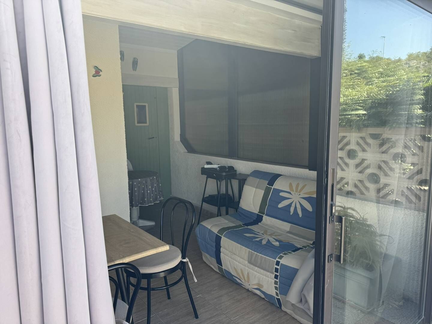 Quarto com mesa de jantar, sofá e uma cadeira. Uma porta dá acesso a outro espaço.