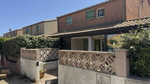 Un edificio residencial con techo de tejas, entrada con reja y detalles de metal ornamental, y un pequeño jardín con plantas en macetas.