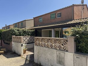 A residential building with a tiled roof, a gated entrance with decorative metalwork, and a small garden area with potted plants. - HOLIDAYLAND VILLA 207 RESIDENCE LES JARDINS D'ULYSSE AIR CONDITIONED 3 BEDROOMS 60 m2 (NARBONNE PLAGE)