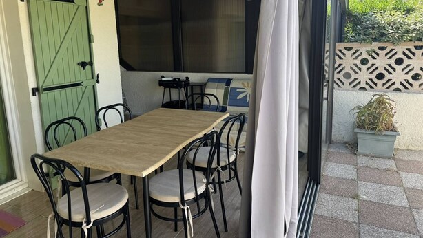 Un patio exterior con mesa y sillas de madera, una puerta verde y un muro decorativo.
