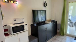 Una cocina compacta con microondas, tostadora y un televisor de pantalla plana sobre un mueble negro.