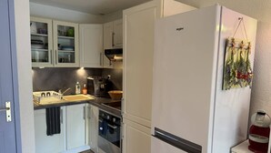 Una cocina compacta con armarios blancos, un lavamanos de acero inoxidable y un refrigerador blanco.
