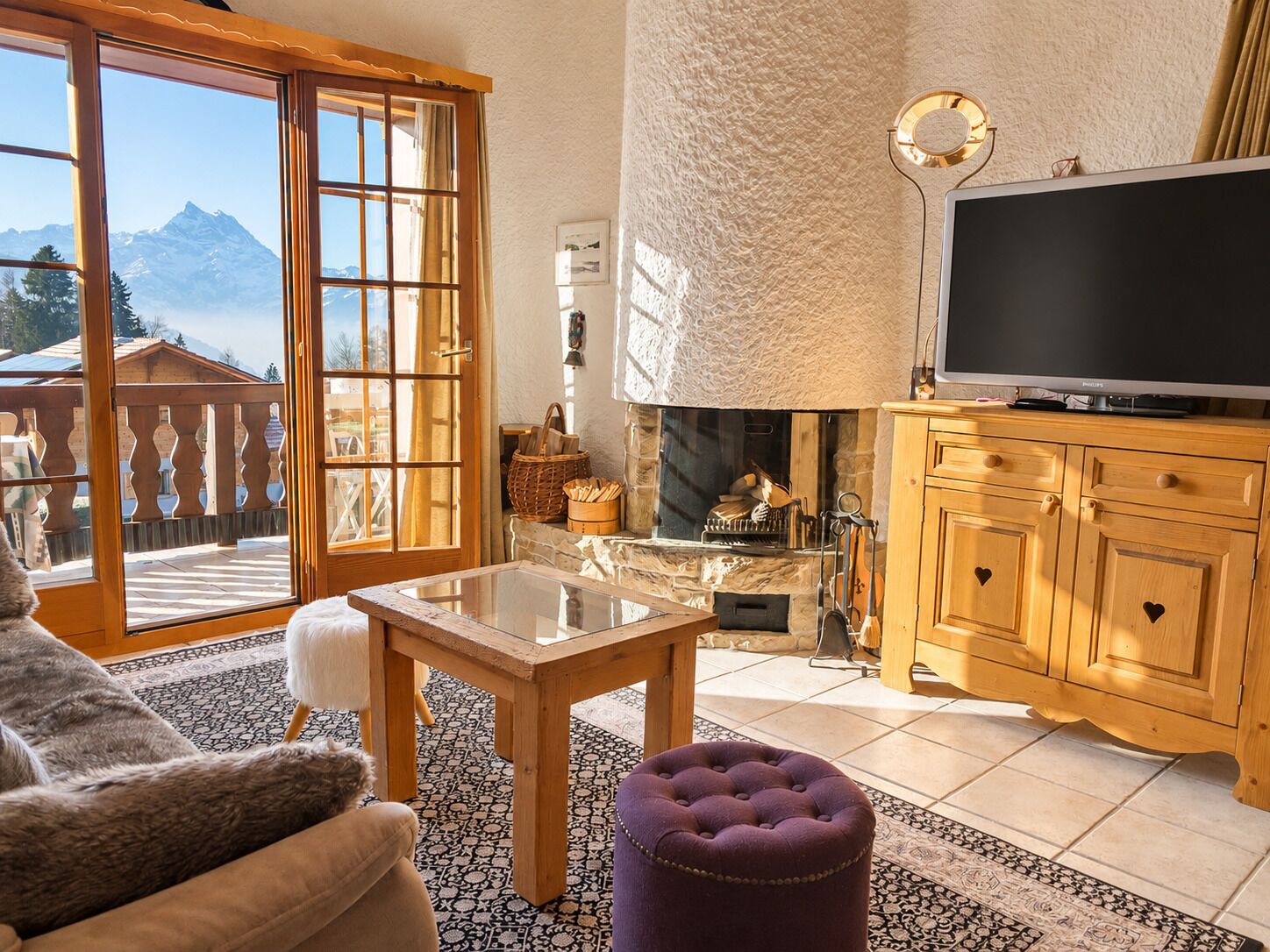 Un salon chaleureux avec une cheminée, un téléviseur et une vue sur les montagnes grâce à de grandes fenêtres.