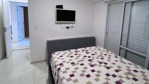Un dormitori amb un llit, una televisió penjada a la paret i un aparell d'aire condicionat sobre el llit.