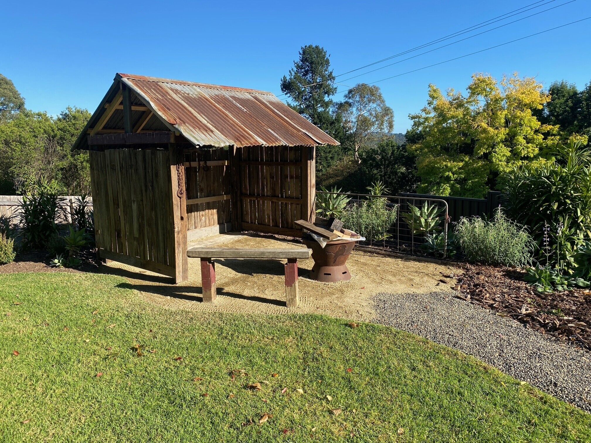 A wooden shed with a slanted roof, a bench, and a planter.