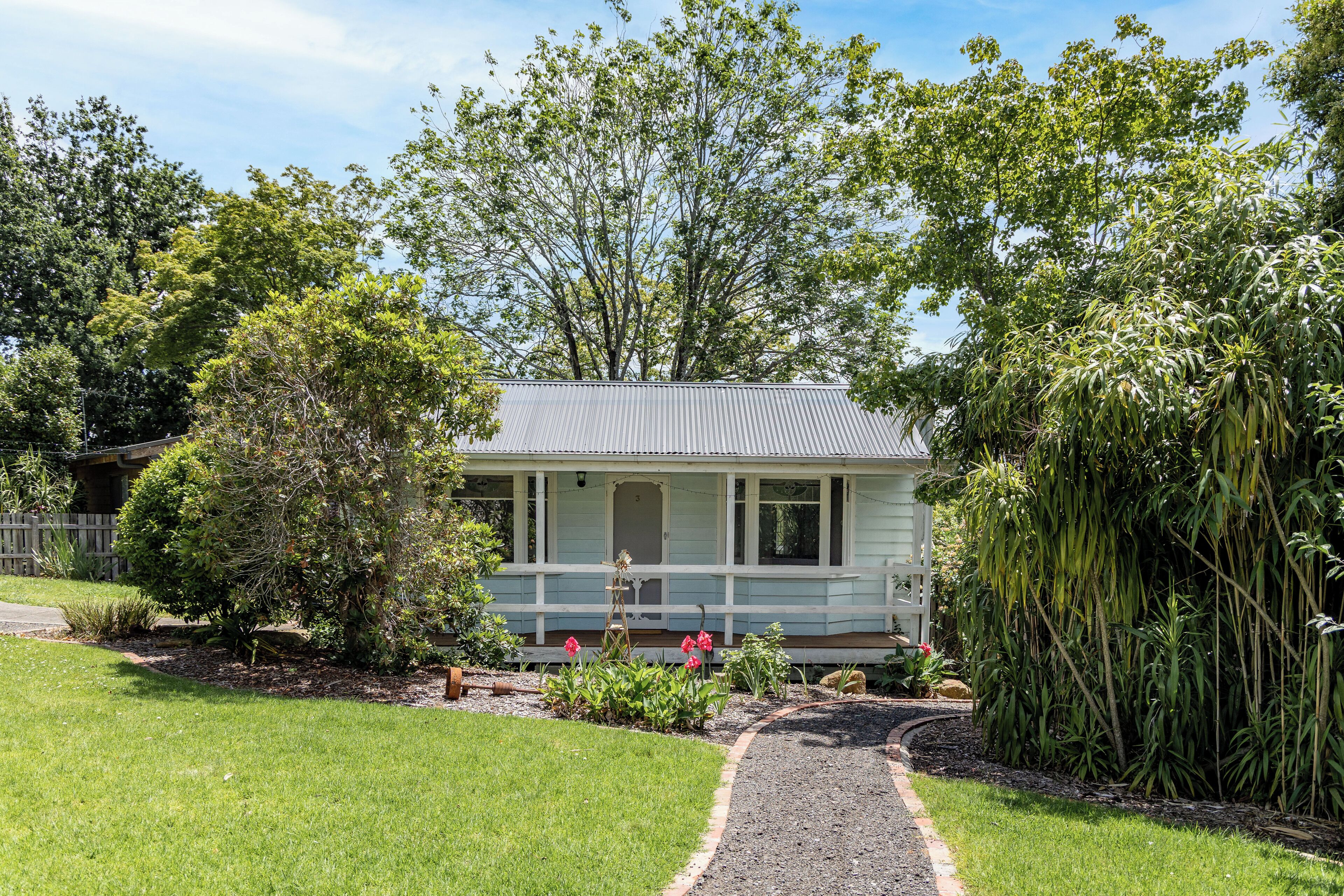 A small, single-story house with a porch, surrounded by a well-maintained garden and trees.