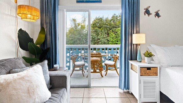 Et værelse med balkon, sofa, bord med stole, lampe og et skilt over døren.