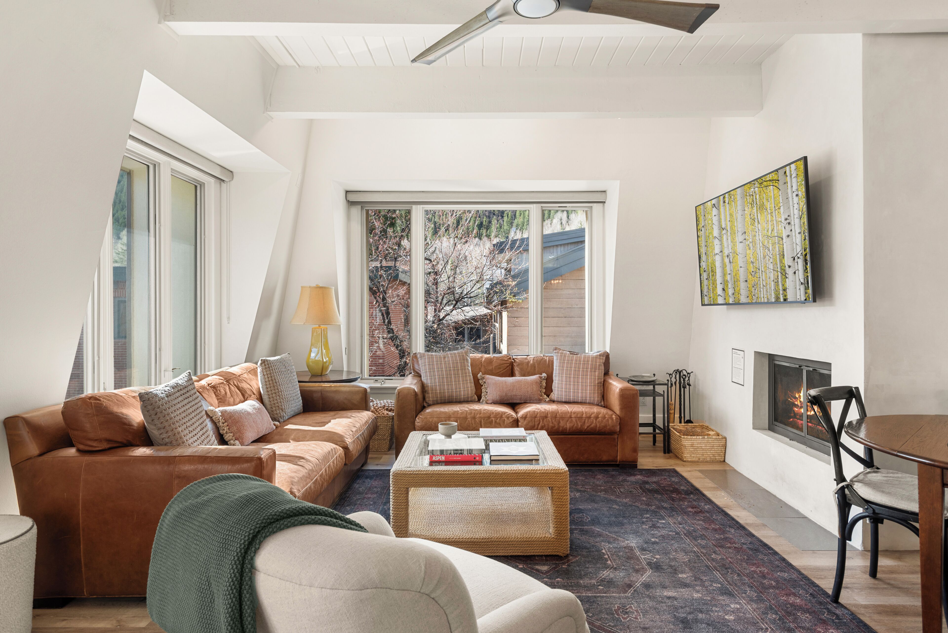 A modern living room with a high ceiling, large windows, a fireplace, and a view of the outdoors.